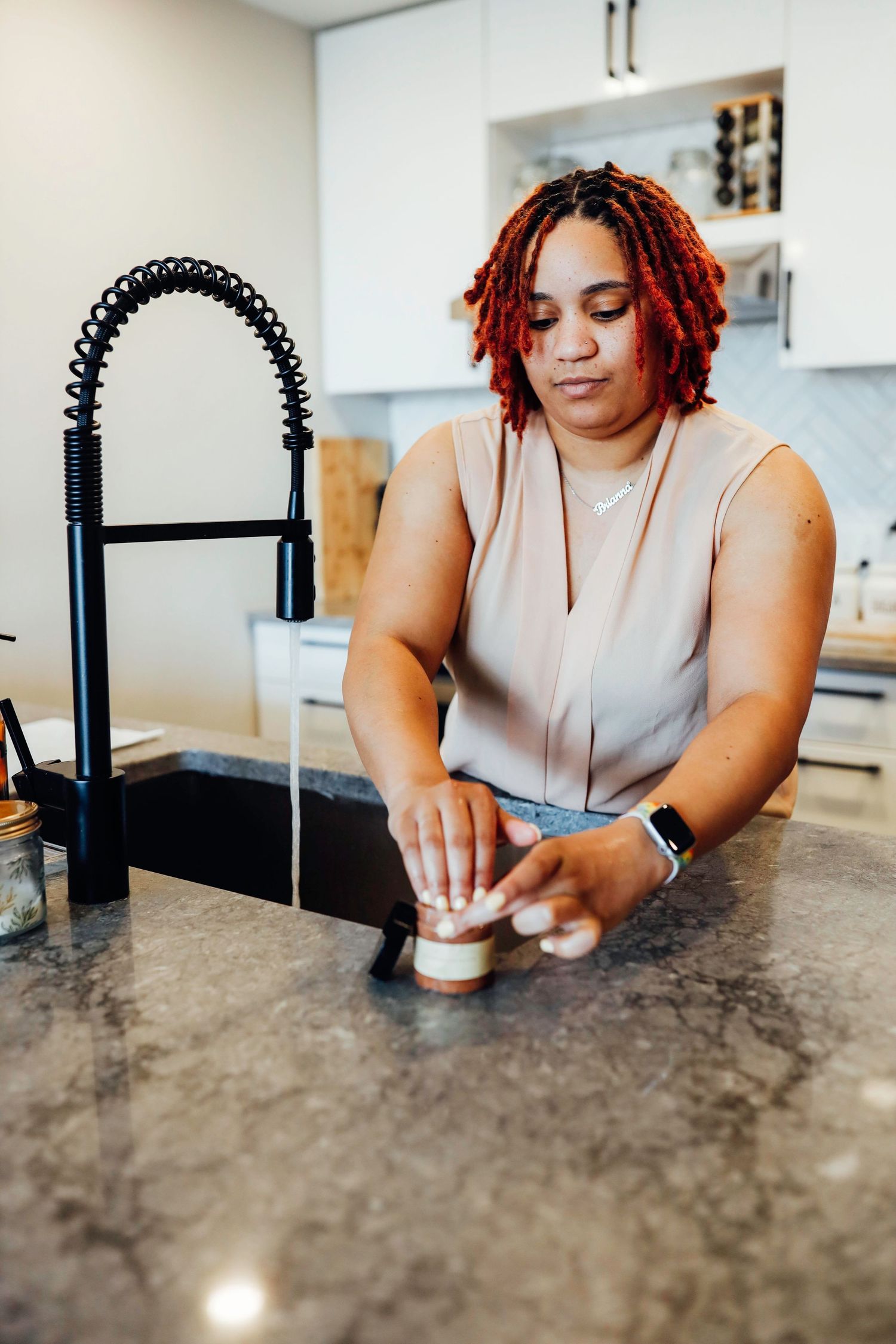 A person with red braided hair works at a granite kitchen counter with a modern black faucet.