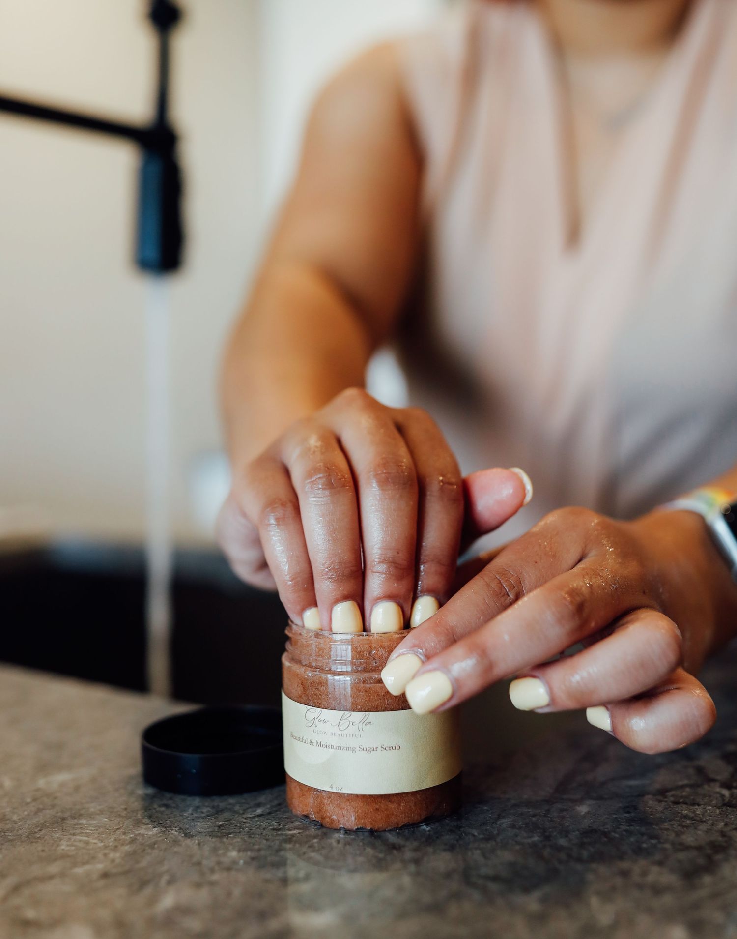 Hands opening a small cosmetic jar on a dark granite countertop.