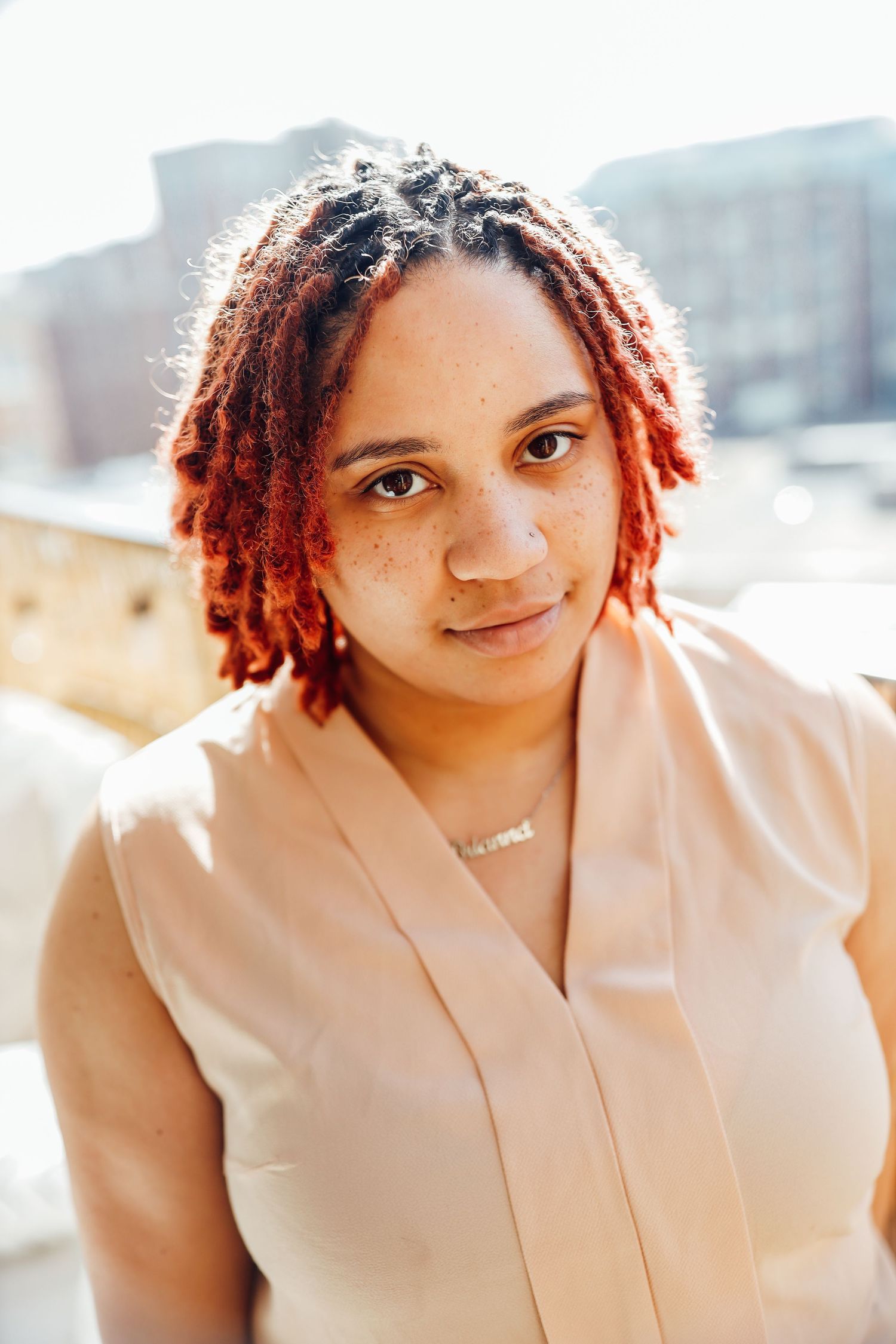 A casual portrait in warm sunlight featuring red braided hair and a beige top.