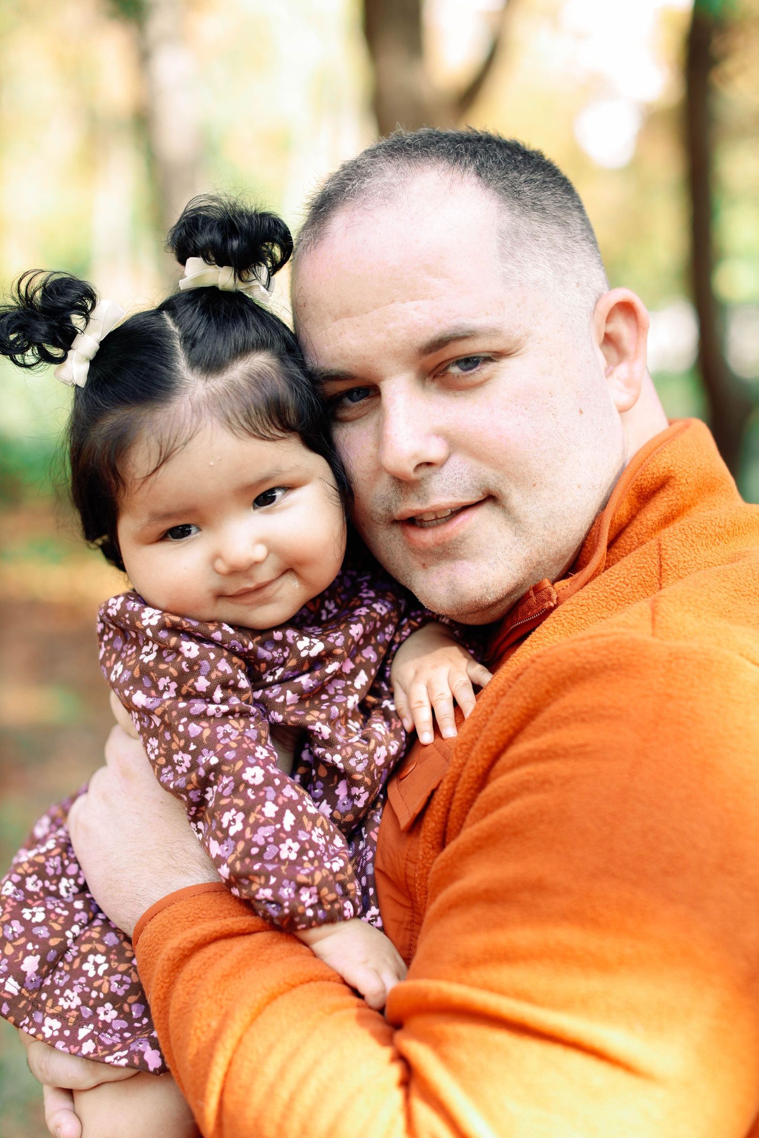 An outdoor portrait showing a person holding a small child in a floral dress.
