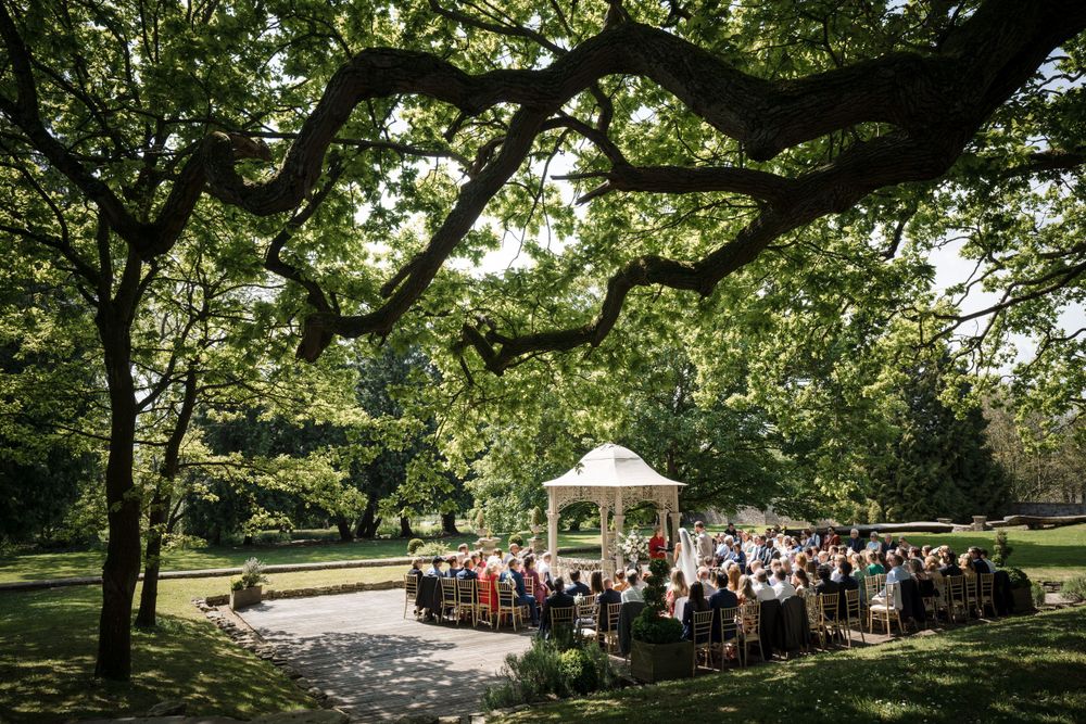 A gathering by a white gazebo for an outdoor wedding ceremony surrounded by lush trees in a park setting, Nova Scotia wedding photographer