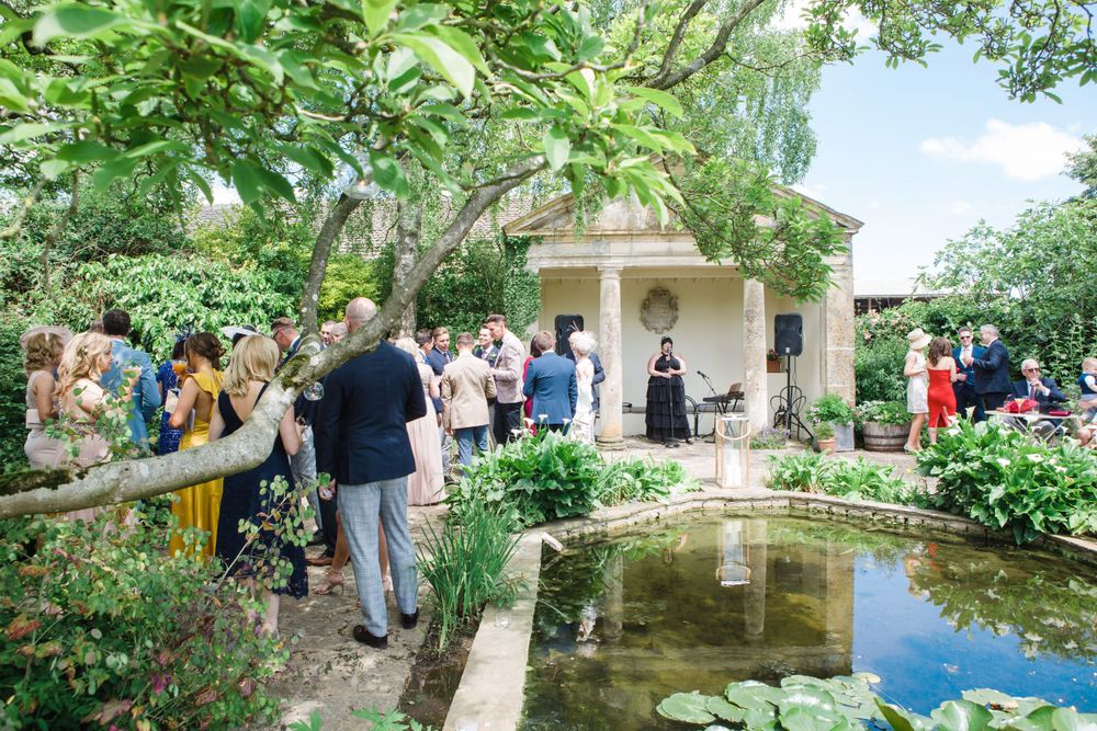 Wedding guests gather around a garden pond surrounded by lush greenery and flowers for Nova Scotia wedding photographer