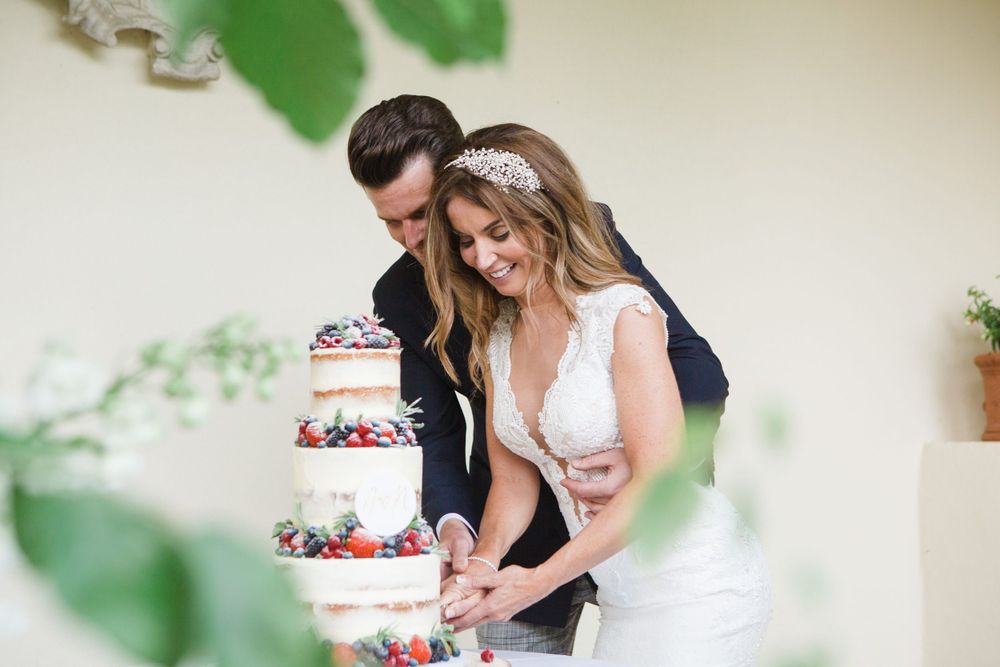 A couple cuts into their elegant three-tiered naked wedding cake during their outdoor reception for Nova Scotia wedding photographer.