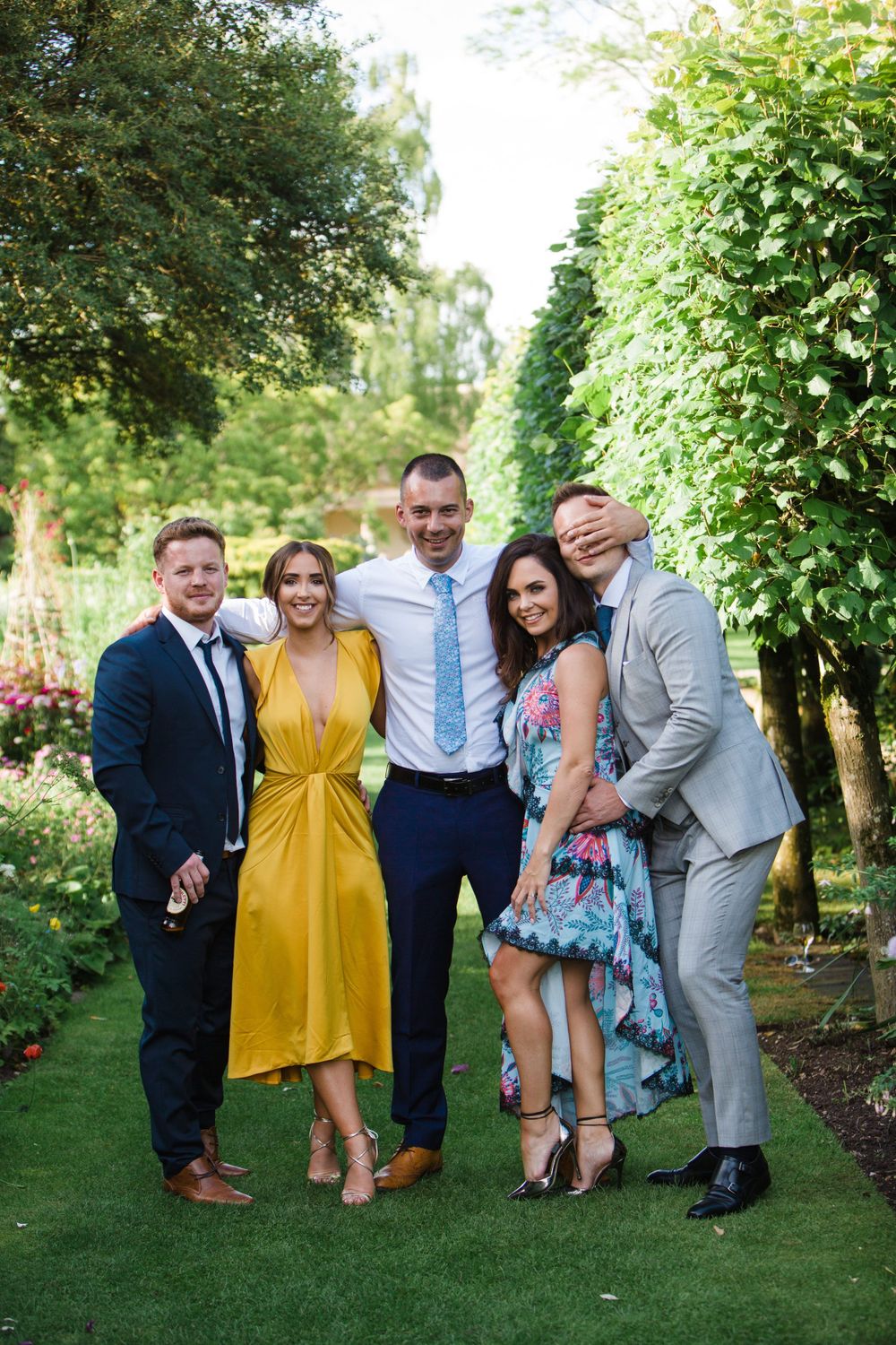 A group in formal attire poses together on a garden path with lush greenery in the background at the Tangled Garden for Nova Scotia wedding