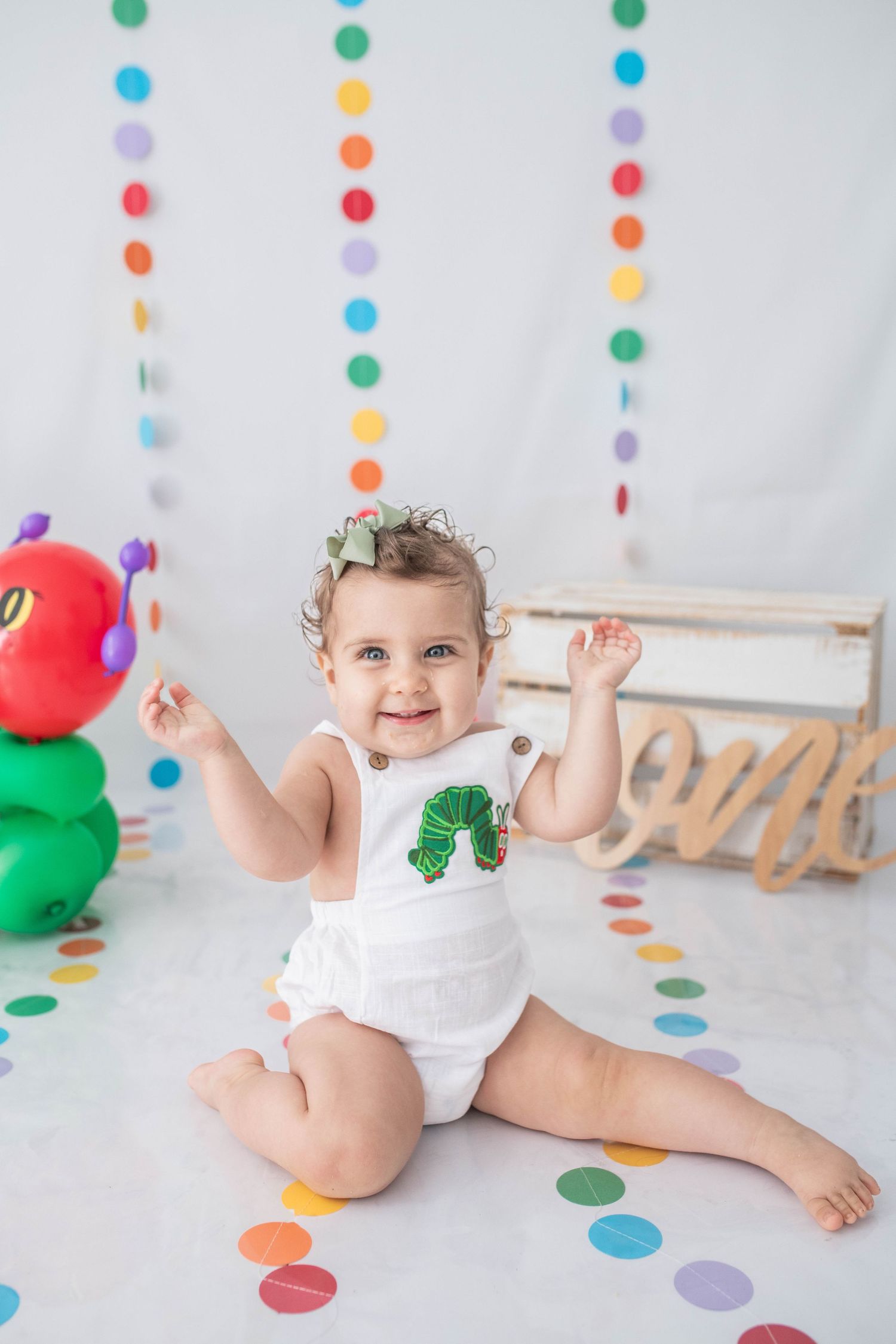 A sweet girl enjoying a caterpillar-themed cake smash, surrounded by adorable setup details, creating fun and memorable moments for her 1st