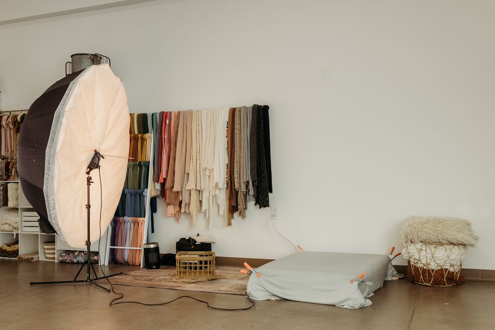 Photography studio with softbox light, colorful fabric swatches on wall, and a cushioned floor mat for product shoots.