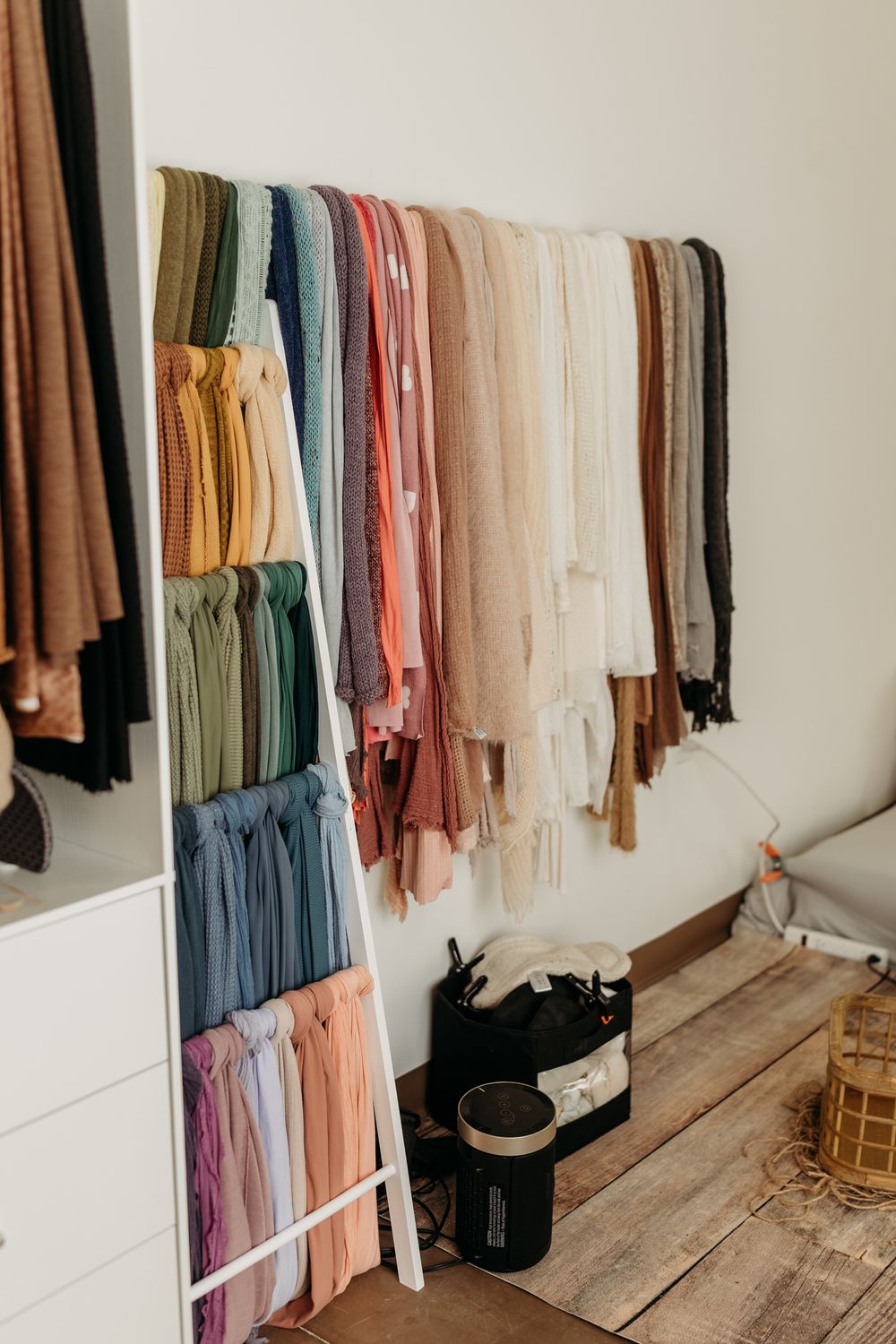 Colorful scarves and clothing neatly organized on a white ladder rack in a bright, modern closet.