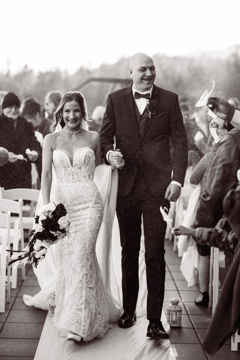 A happy couple walking down an outdoor wedding aisle as guests look on during their black and white ceremony.