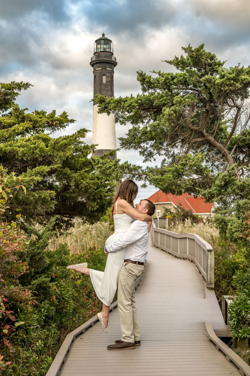 A lighthouse keeper climbs the exterior walkway of a white coastal lighthouse on a cloudy day.