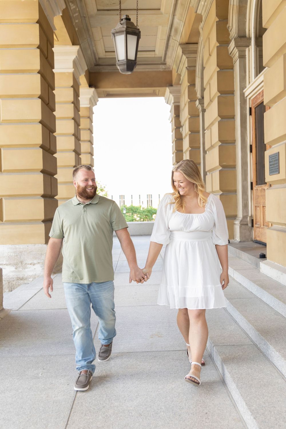 Engaged couple walking on the front outdoor steps of the Iowa State Capital Building.