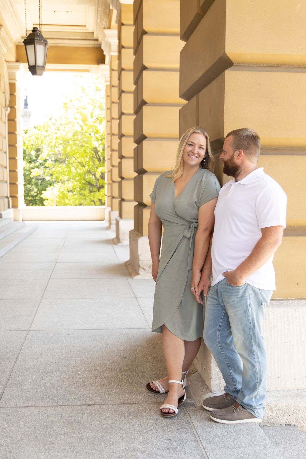 Couple smiling at each other during an engagement session on the front archway of the Iowa State Capital.