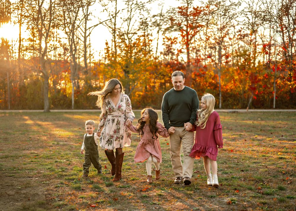 A family walks together through a golden autumn field during sunset while holding hands.