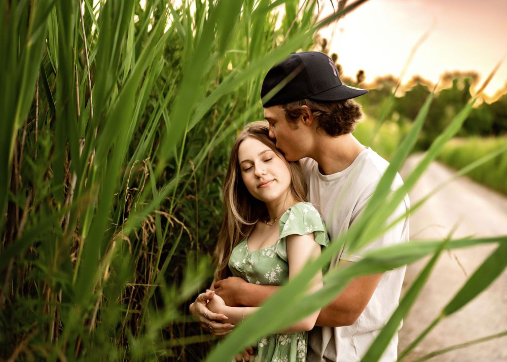 Couple embraces in romantic summer setting among tall reeds during golden hour sunset.