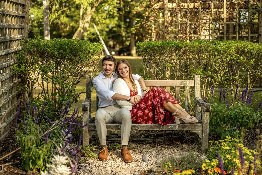 Couple sitting on a garden bench surrounded by blooming spring flowers and lush greenery in a peaceful outdoor setting.