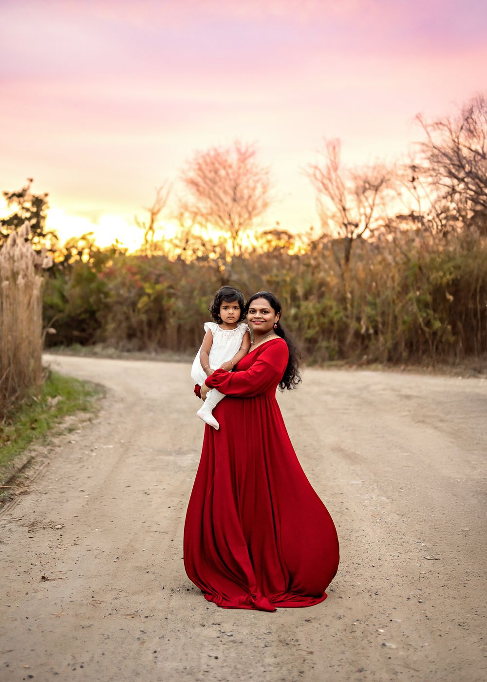 Two figures in flowing red dresses dance together on a dirt path at sunset creating a dreamy silhouette.