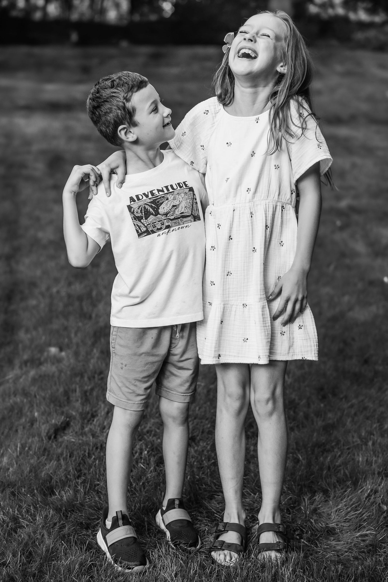 Black and white candid photo of two children sharing a laugh together outdoors.