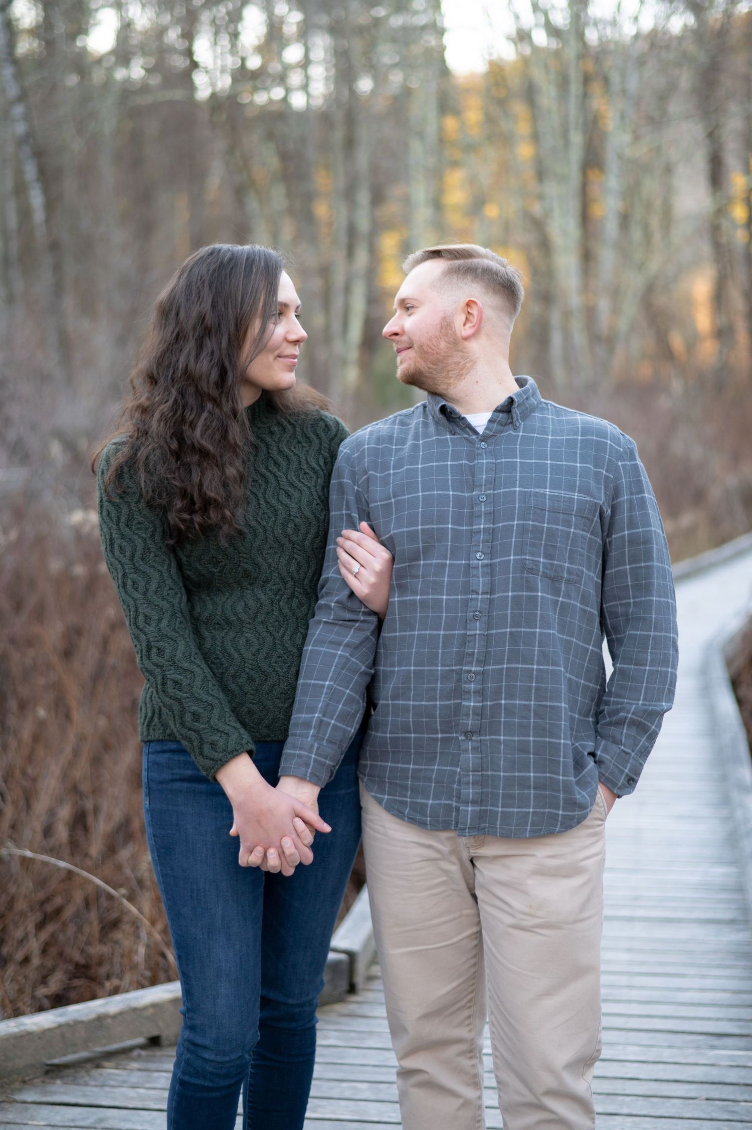 A couple shares a romantic moment while walking along a wooden boardwalk path through autumn woods.