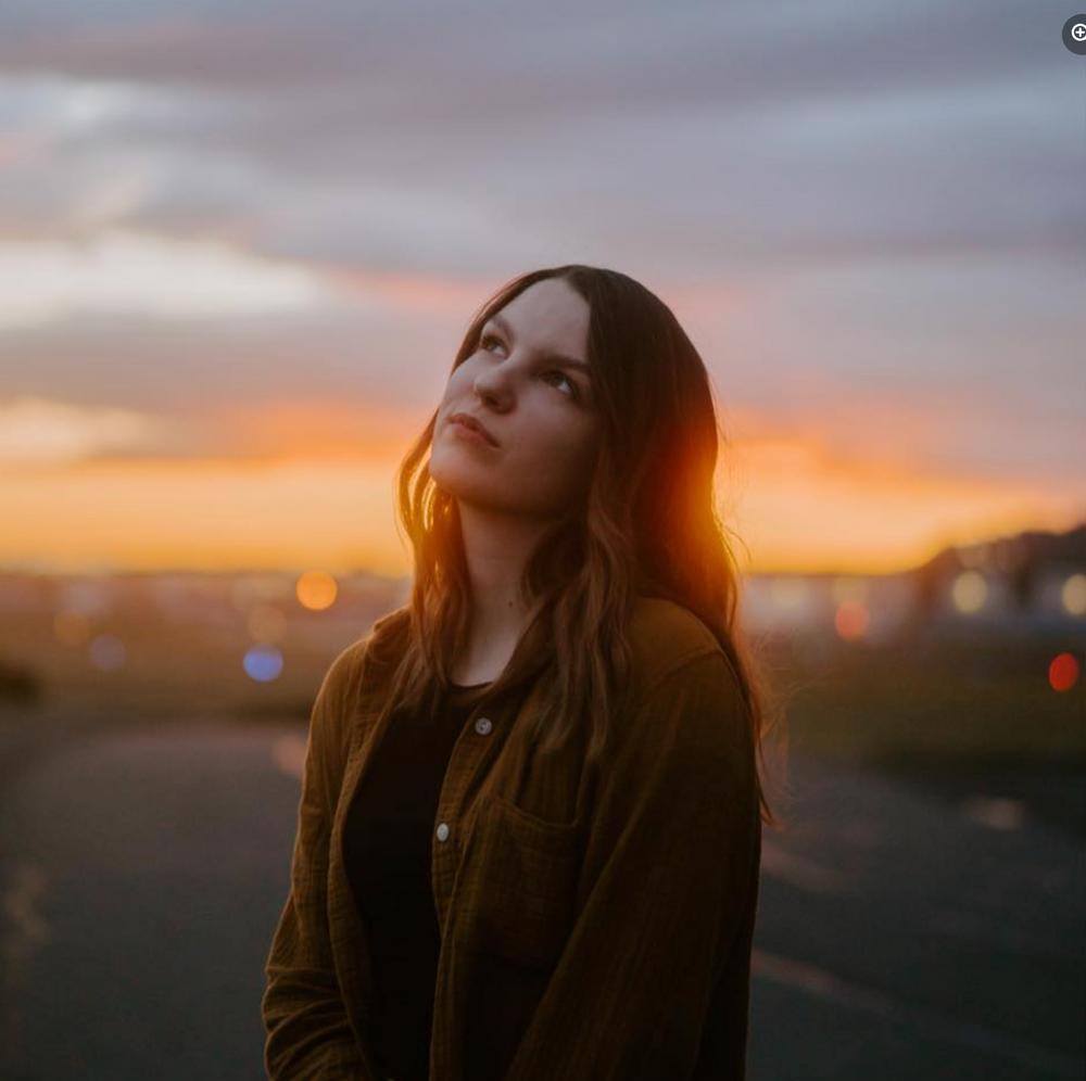 A dreamy portrait against a vibrant sunset sky with glowing bokeh lights in the background.