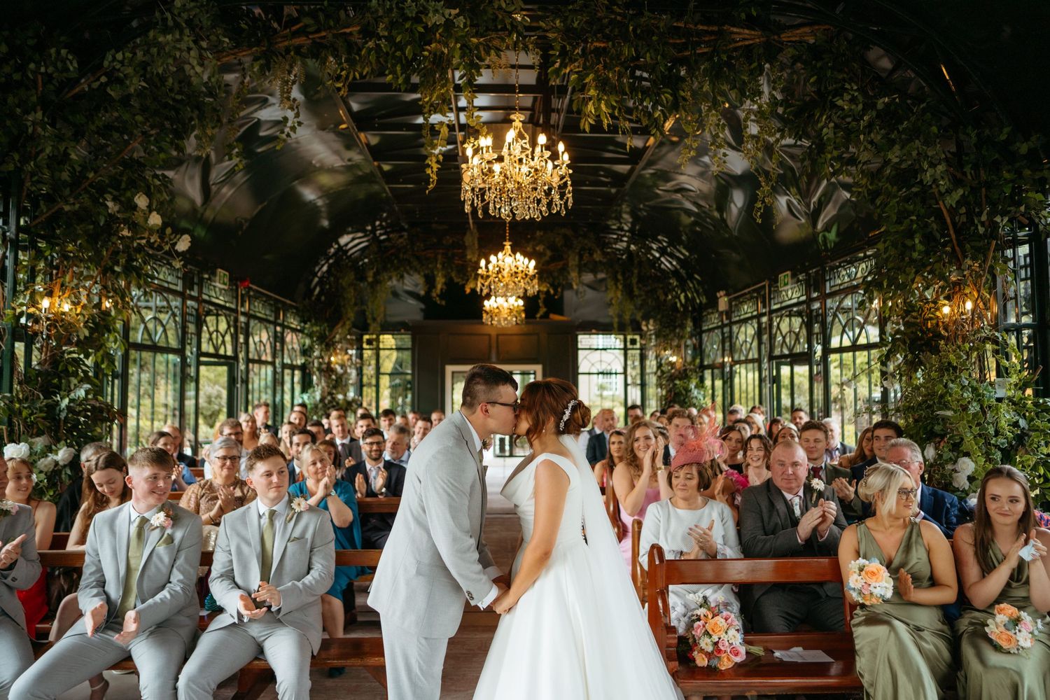 Wedding celebration in an elegant green-walled venue with chandeliers and gathered guests.