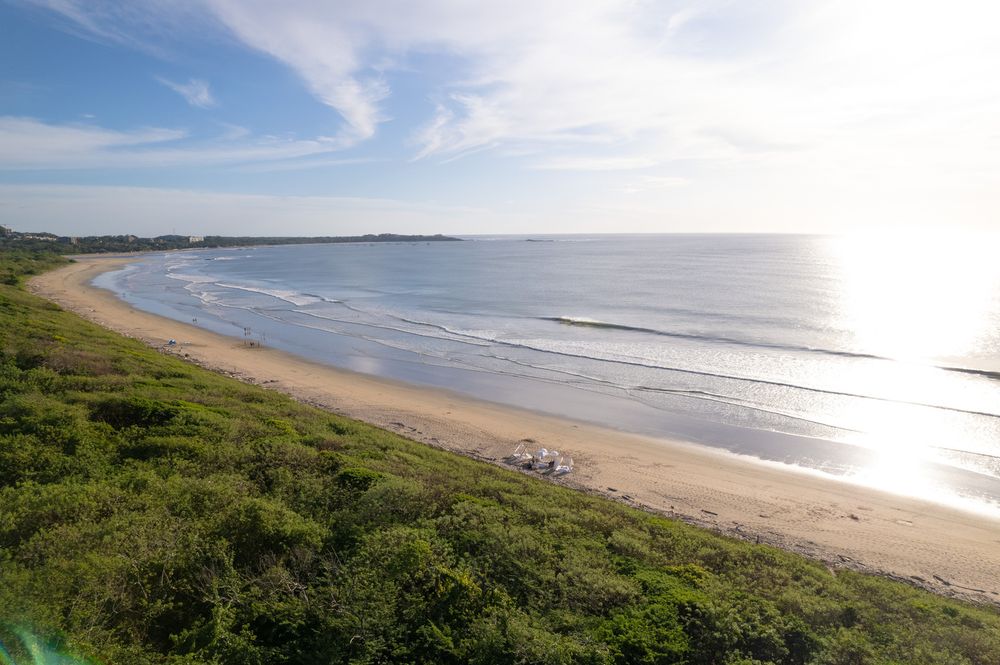 Scenic coastal landscape with gentle waves washing onto a curved sandy beach under bright blue skies.