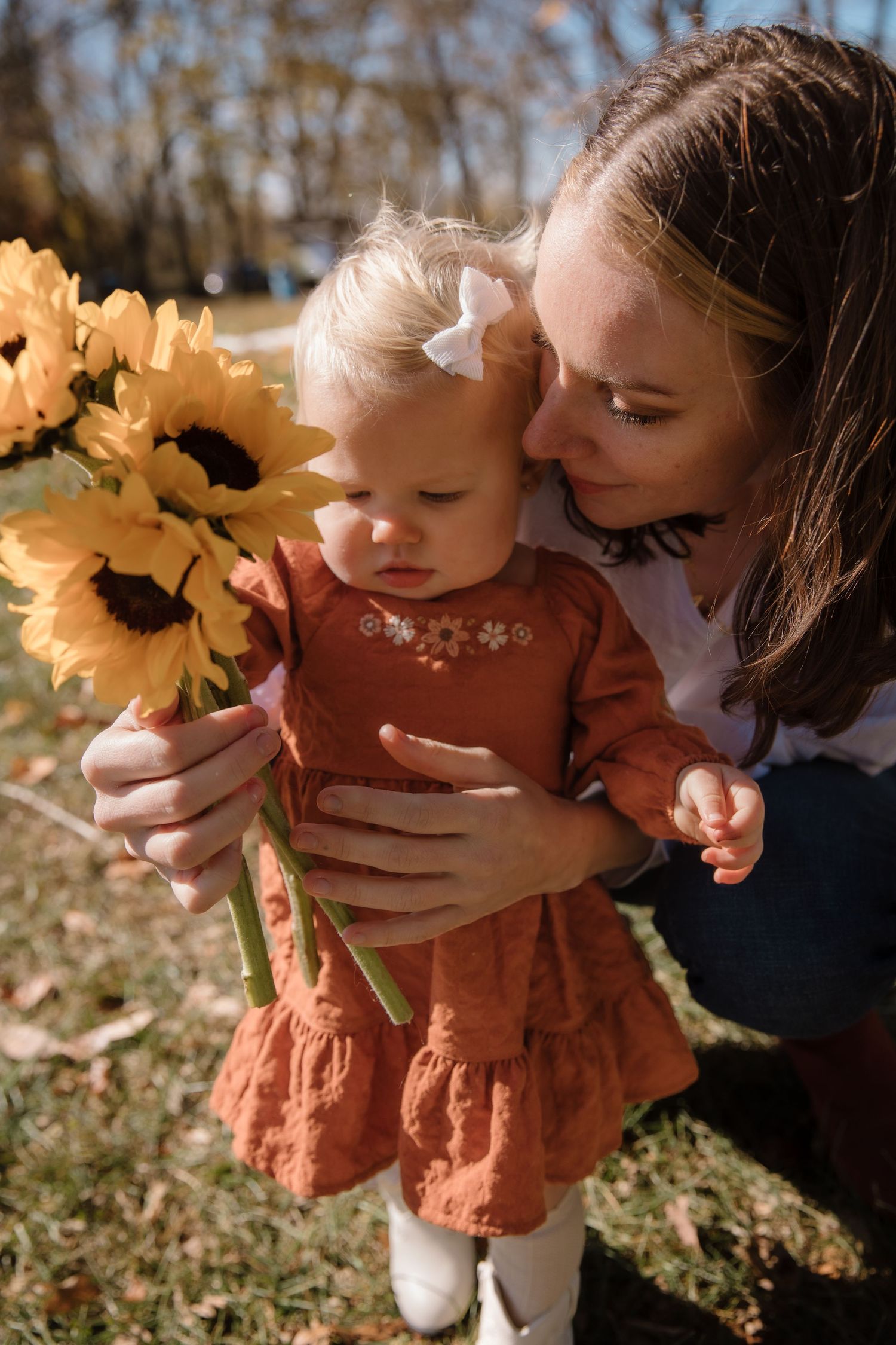 A tender moment shared with a small child while looking at bright yellow sunflowers in a sunny outdoor setting.