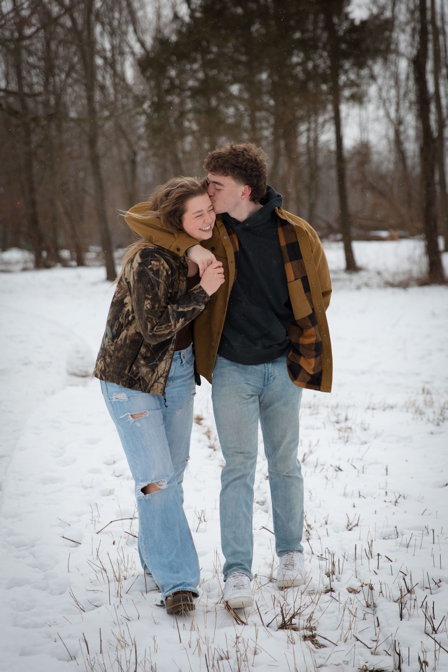 A playful winter moment between two people walking through snow-covered woods.