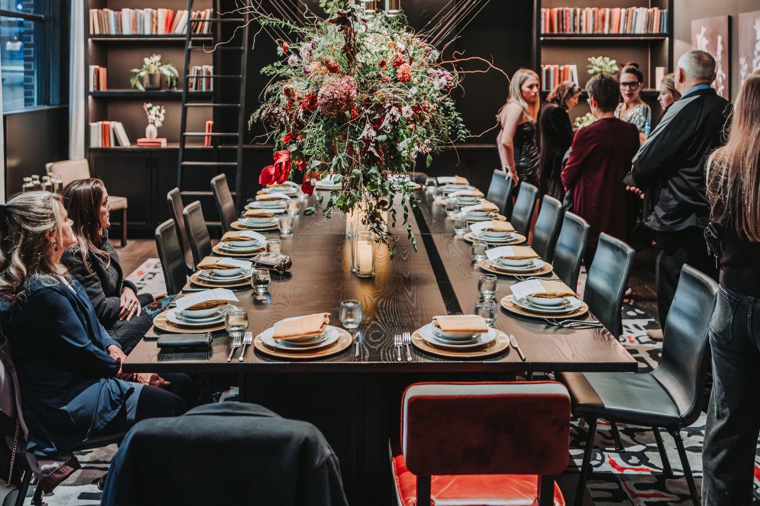 An elegant dinner table setting with a floral centerpiece in a library-themed restaurant with bookshelves.  Located at the Canopy Hotel.