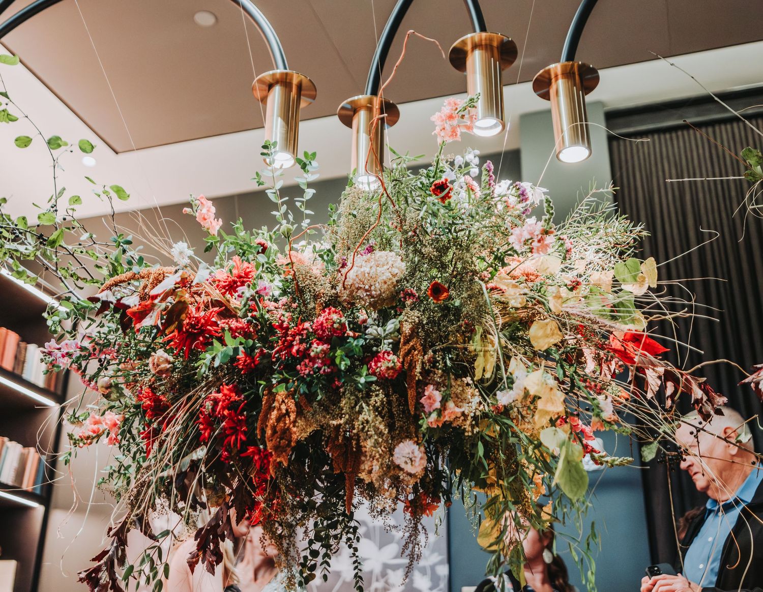 A stunning floral chandelier with red and pink blooms hanging from copper lighting fixtures in an indoor space.  Located at the Canopy Hotel