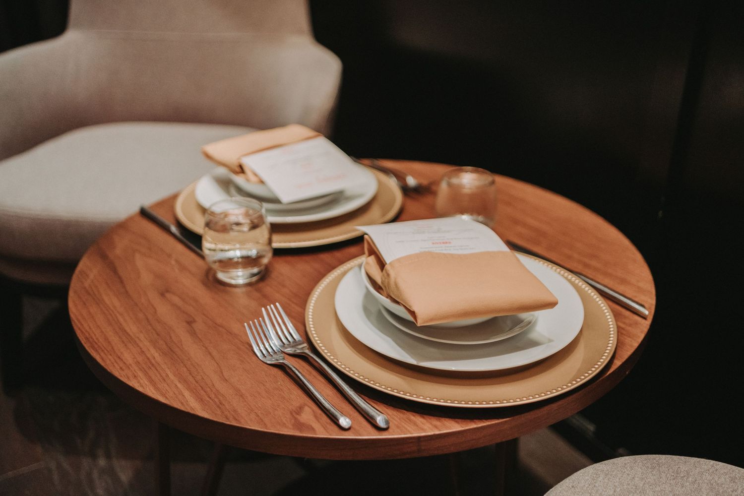 Place setting with white plates and napkins on a round wooden table with silverware and glassware.  Located at the Canopy Hotel in Portland.