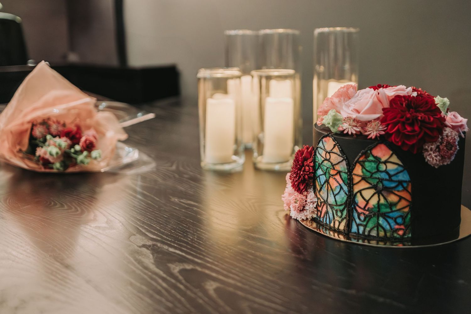Black cake decorated with vibrant red roses and stained glass butterfly design sits on table with candles and flowers nearby.  Canopy Hotel.