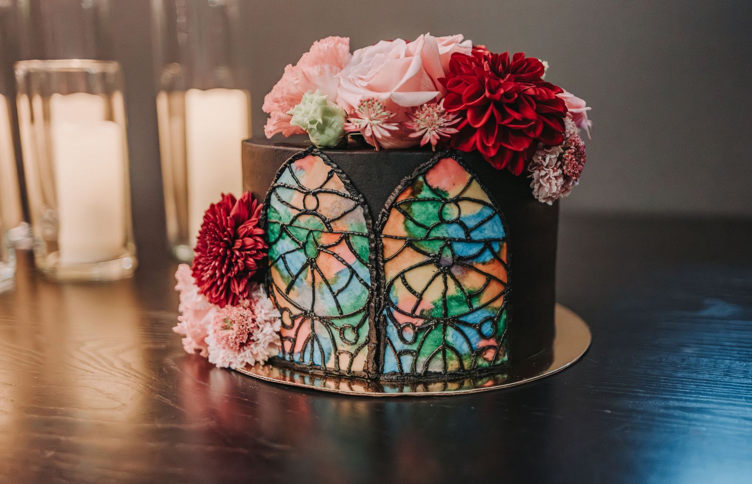 A dark cake decorated with floral accents and stained glass window design illuminated with blue and green colors.  Canopy Hotel.