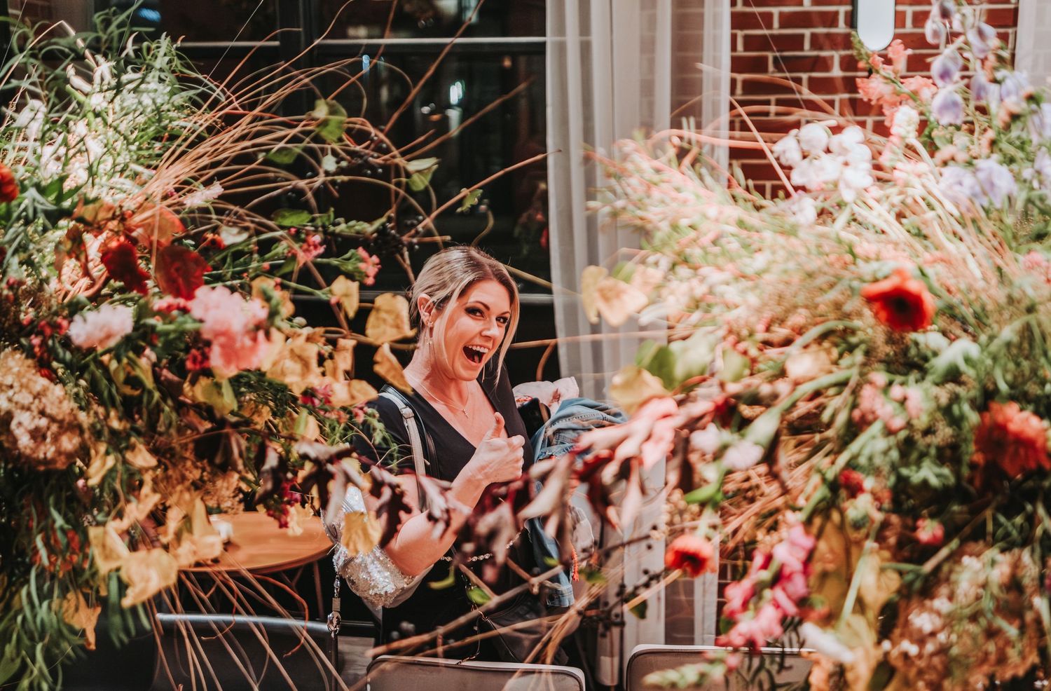 A serene scene with autumn flowers and foliage framing a figure reading on a porch by a brick building.  Canopy Hotel in Portland, Maine.