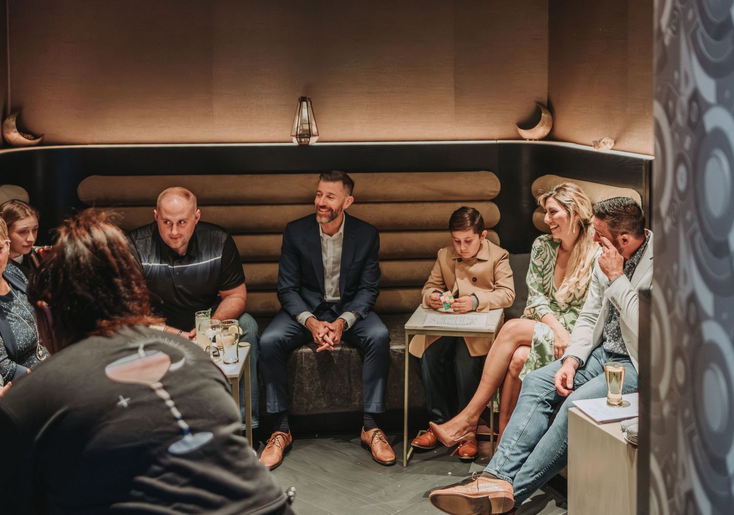 Group of friends gathered on a curved lounge booth having casual conversation during a night out prior to a wedding being held in Portland.