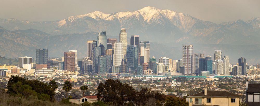 Panoramic view of Los Angeles skyline with snow-capped mountains in the background.