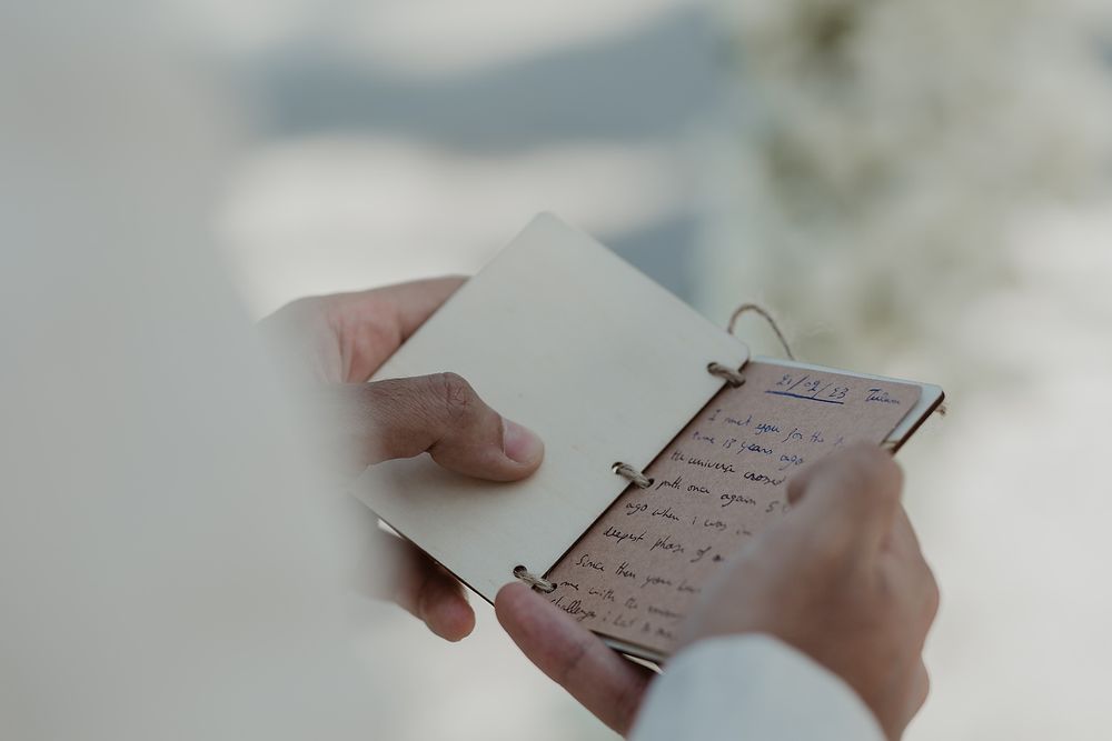 A person reviewing notes or writing in a small paper notebook with a ring binder against a blurred background.