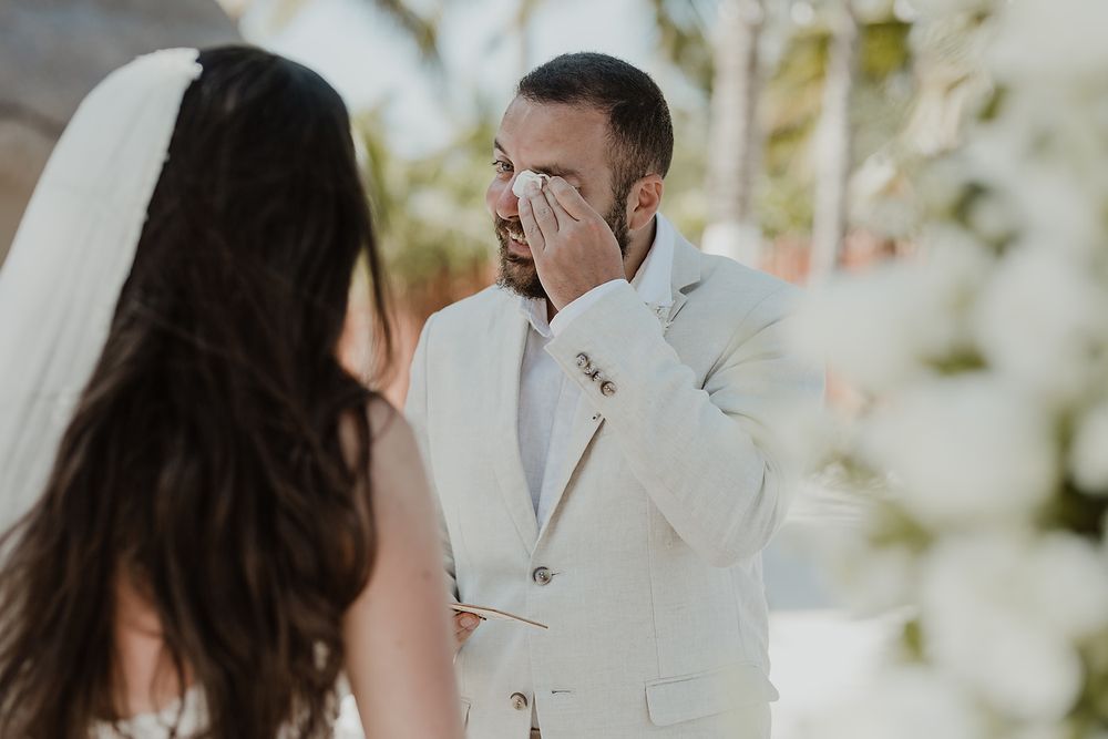 A joyful wedding couple interacts sweetly during their outdoor garden ceremony surrounded by white flowers.