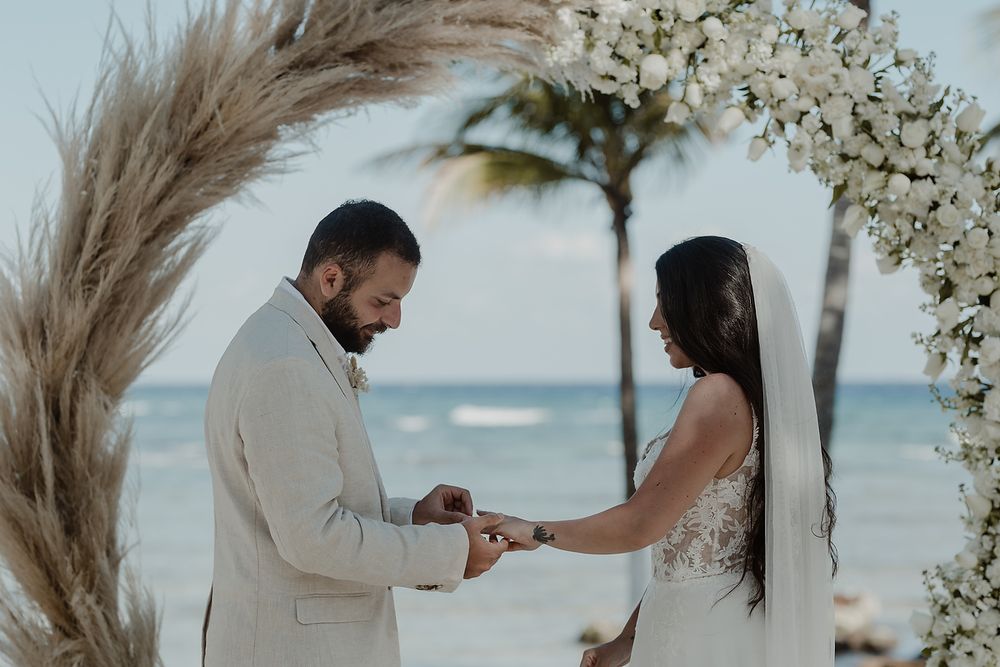 Romantic beachside wedding ceremony with pampas grass arch on a tropical shore with waves crashing in the background.
