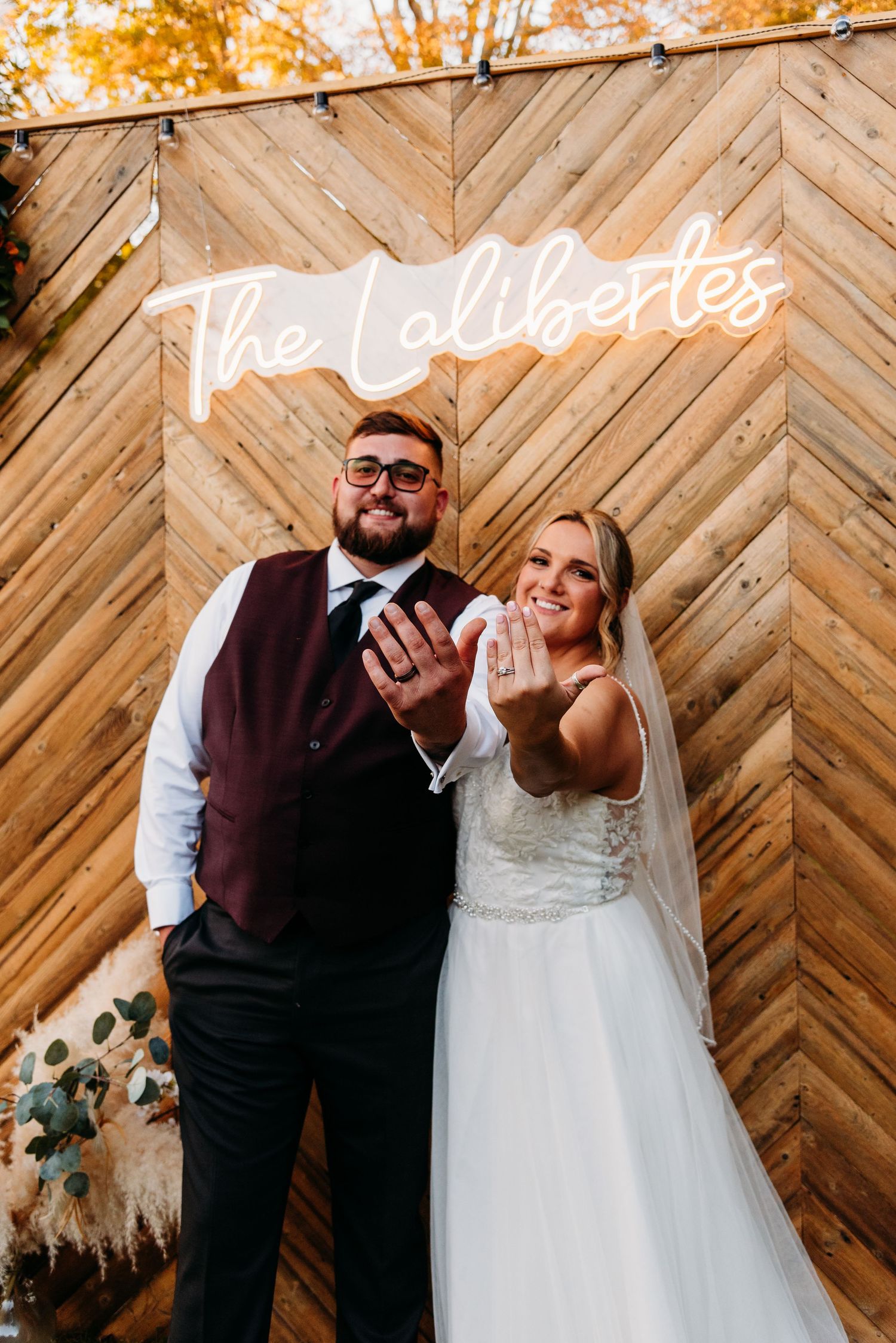 Newlywed couple showing rings under glowing neon sign against wooden wall in Connecticut.