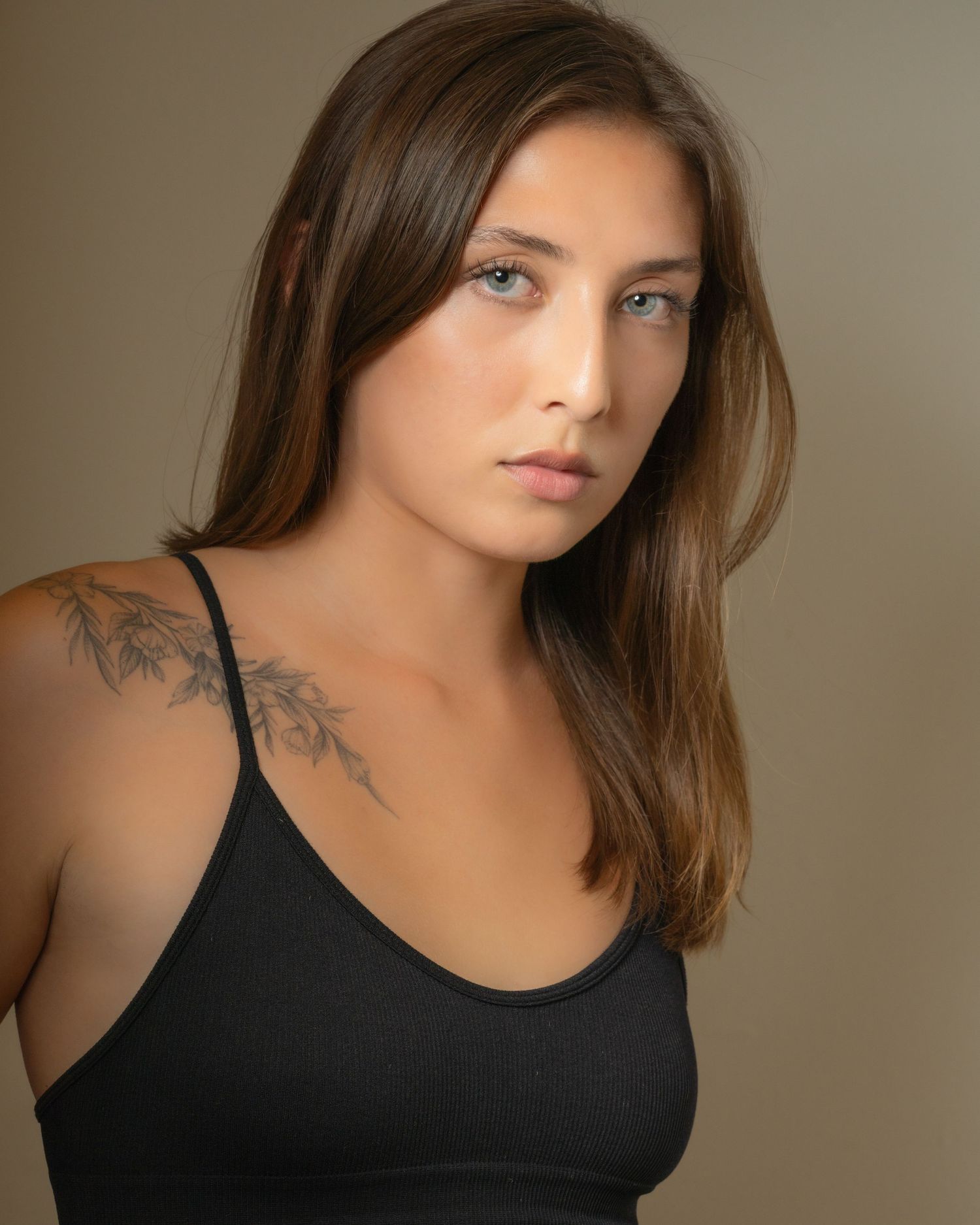 Portrait of woman with tattoo wearing black tank top against neutral background.