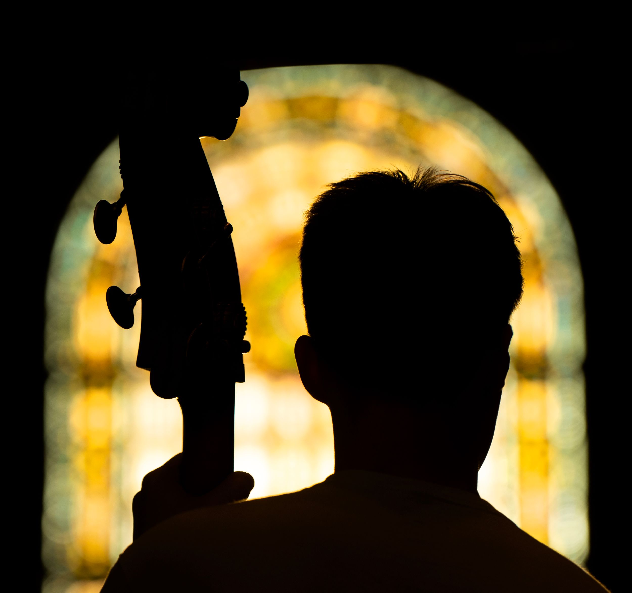 A stand up bass musician is silhouetted against stained glass windows.