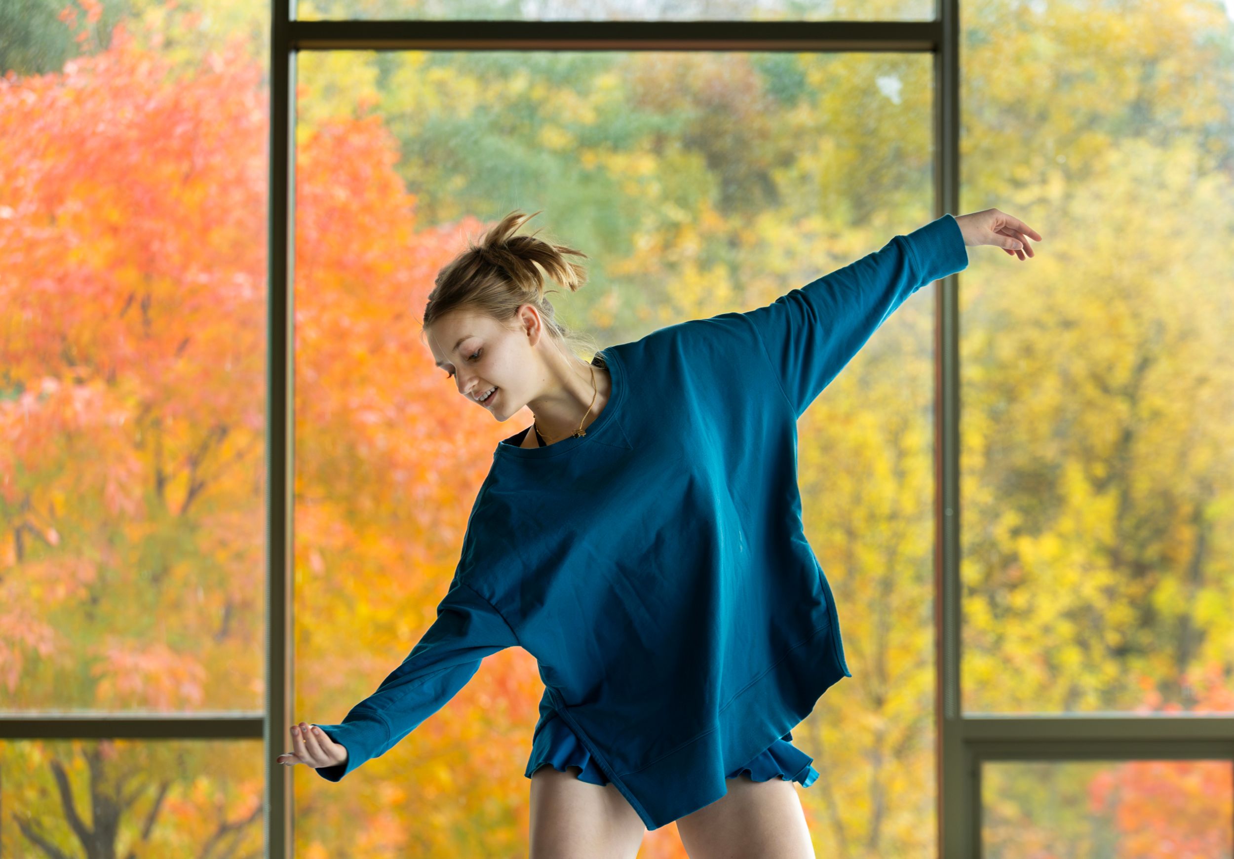 A dancer performs in front of large windows with autumn leaves showing.