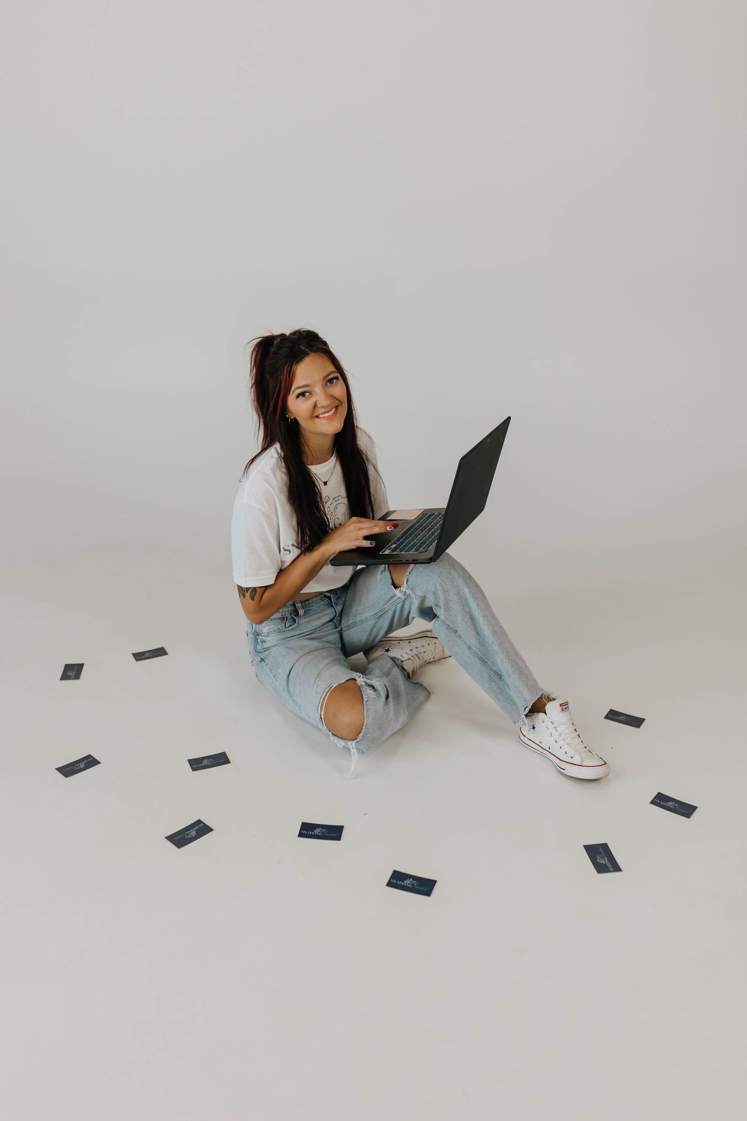 A person in casual attire sits on the floor reading a book while surrounded by scattered papers in a minimalist setting.