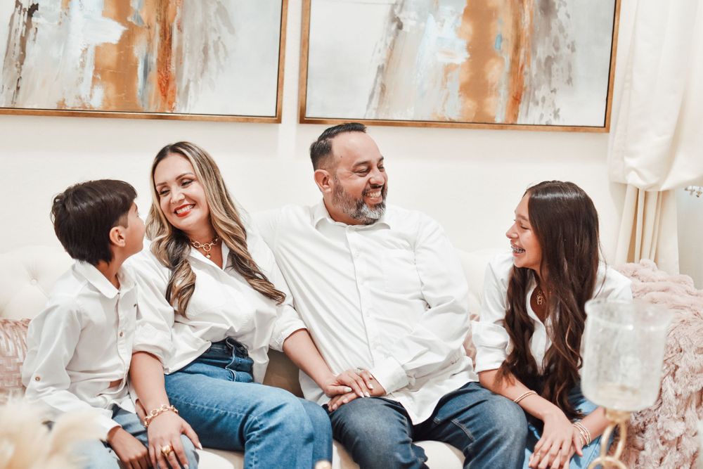 Happy family of four laughing together on a white sofa in a bright living room.