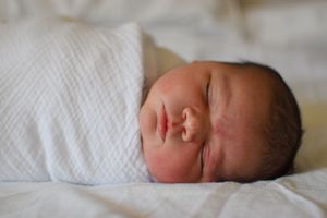 Peaceful newborn baby sleeping soundly swaddled in soft white blanket on bed.