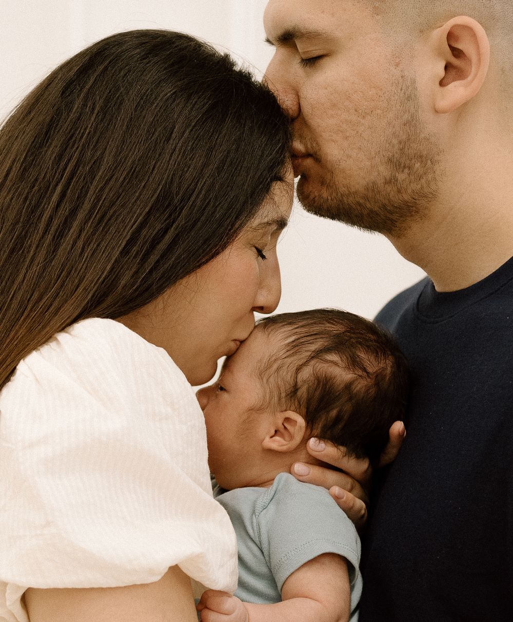 A couple tenderly kisses their newborn baby, sharing a heartfelt family moment together.