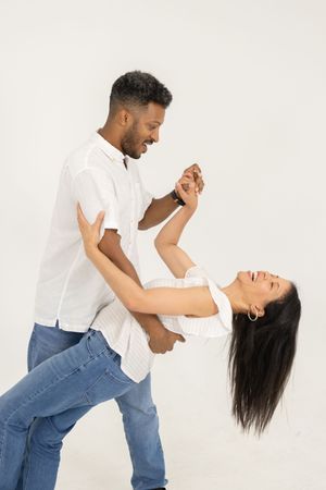 A joyful couple dancing together, man in white shirt and jeans dipping laughing woman with long dark hair.