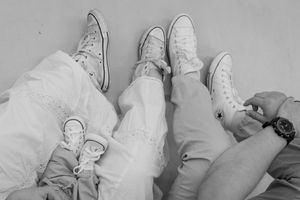Three people lying down wearing classic white Converse Chuck Taylor sneakers in a black and white photo.