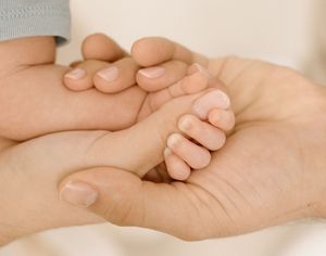 A newborn baby's tiny hand gently resting in the cupped hands of a parent, symbolizing love and care.