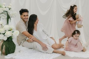 A happy family poses for a maternity photo shoot with two young daughters in a soft white studio setting.
