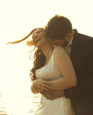 A couple embraces intimately in golden sunlight during a romantic beachside photoshoot.